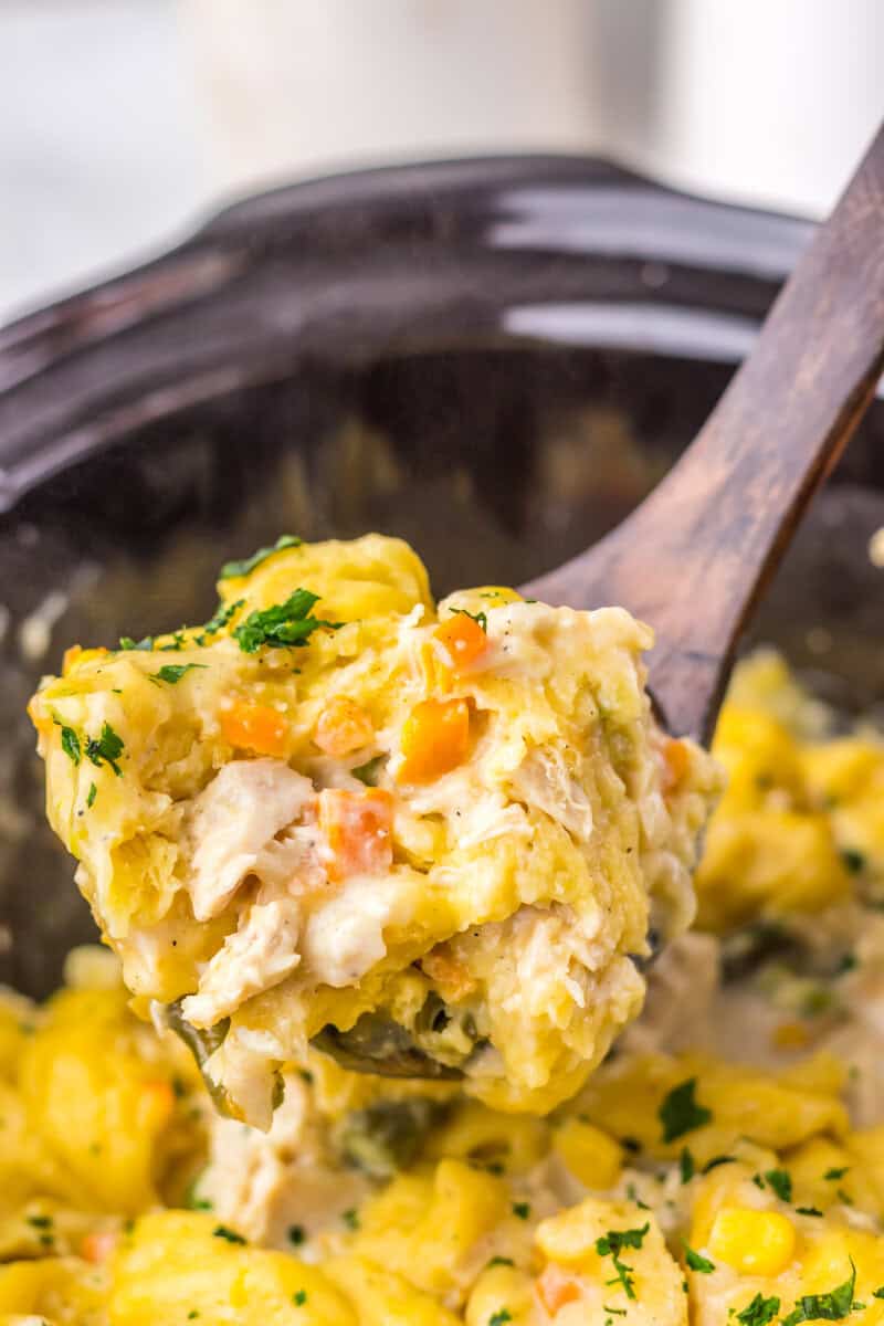 A wooden spoon lifting a serving of slow cooker chicken and dumplings from a Crock Pot.
