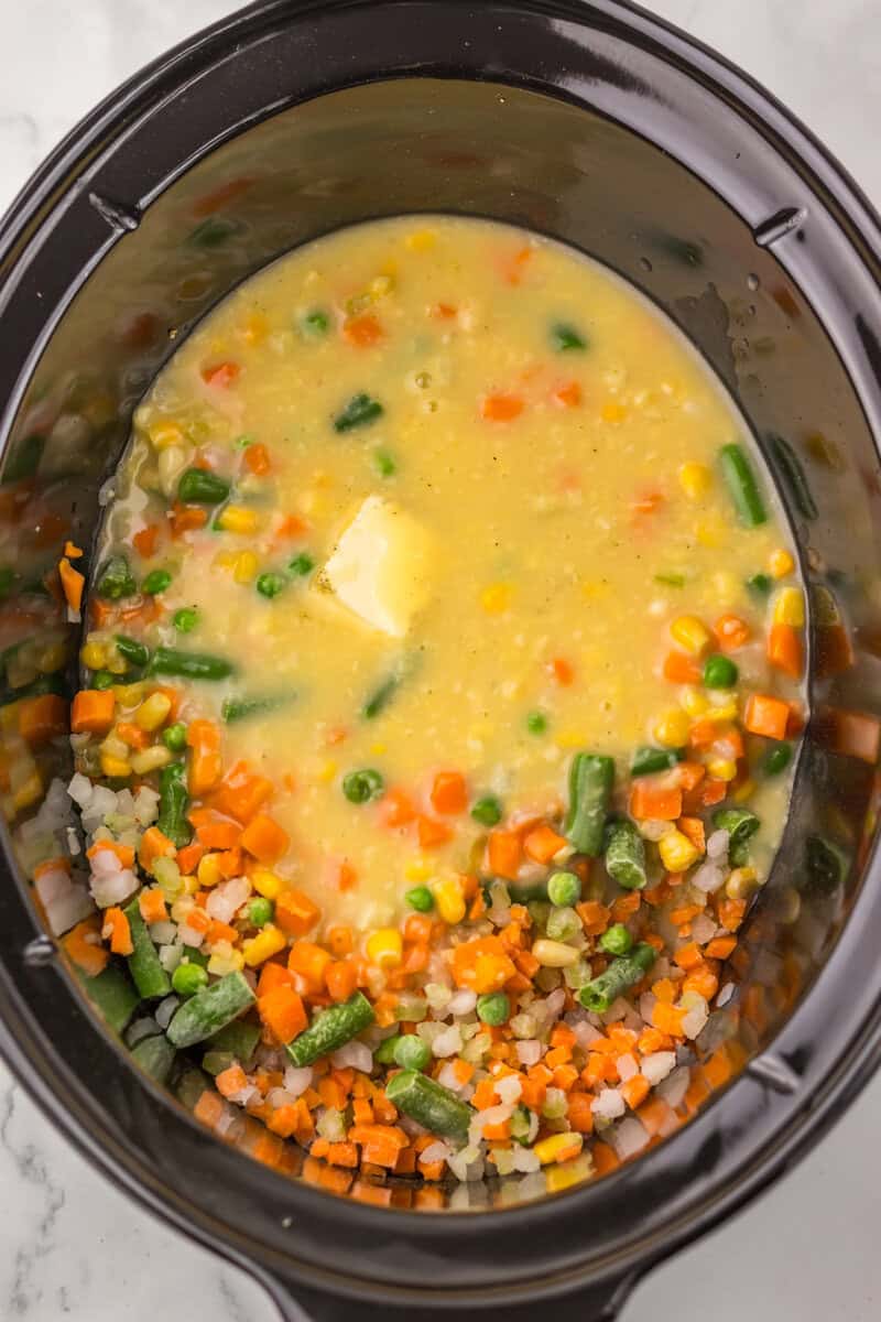 Frozen vegetables, butter, and condensed soup in a black slow cooker.