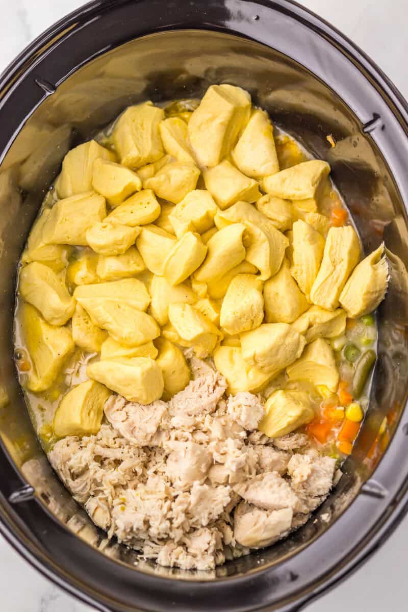 Dough, chicken, and vegetables in a black slow cooker with broth.