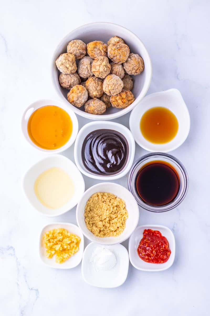 Metballs, hoisin sauce, garlic, sesame oil, soy sauce, chili garlic sauce, and other ingredients in individual bowls on a light surface.