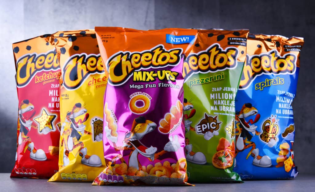 Five brightly colored bags of Cheetos snacks are displayed upright in a row, featuring various flavors and cartoon mascot designs on the packaging, prompting snack lovers to wonder: are Cheetos gluten free?.