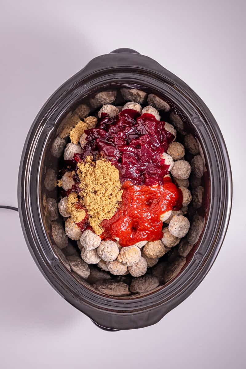 A slow cooker with meatballs, brown sugar, and two sauces.