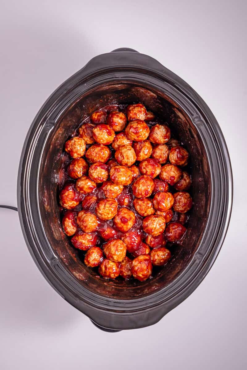 A slow cooker with meatballs and sauce.