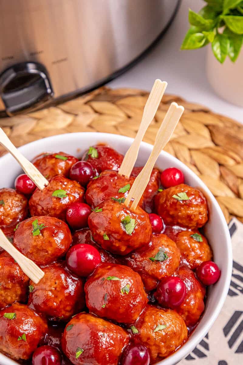 A white bowl of cranberry meatballs with toothpicks stick in severa;.