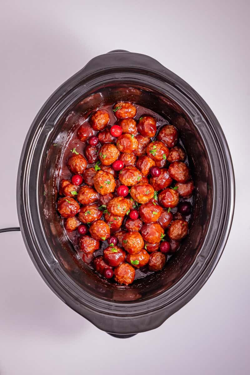 A slow cooker with meatballs and whole cranberries.