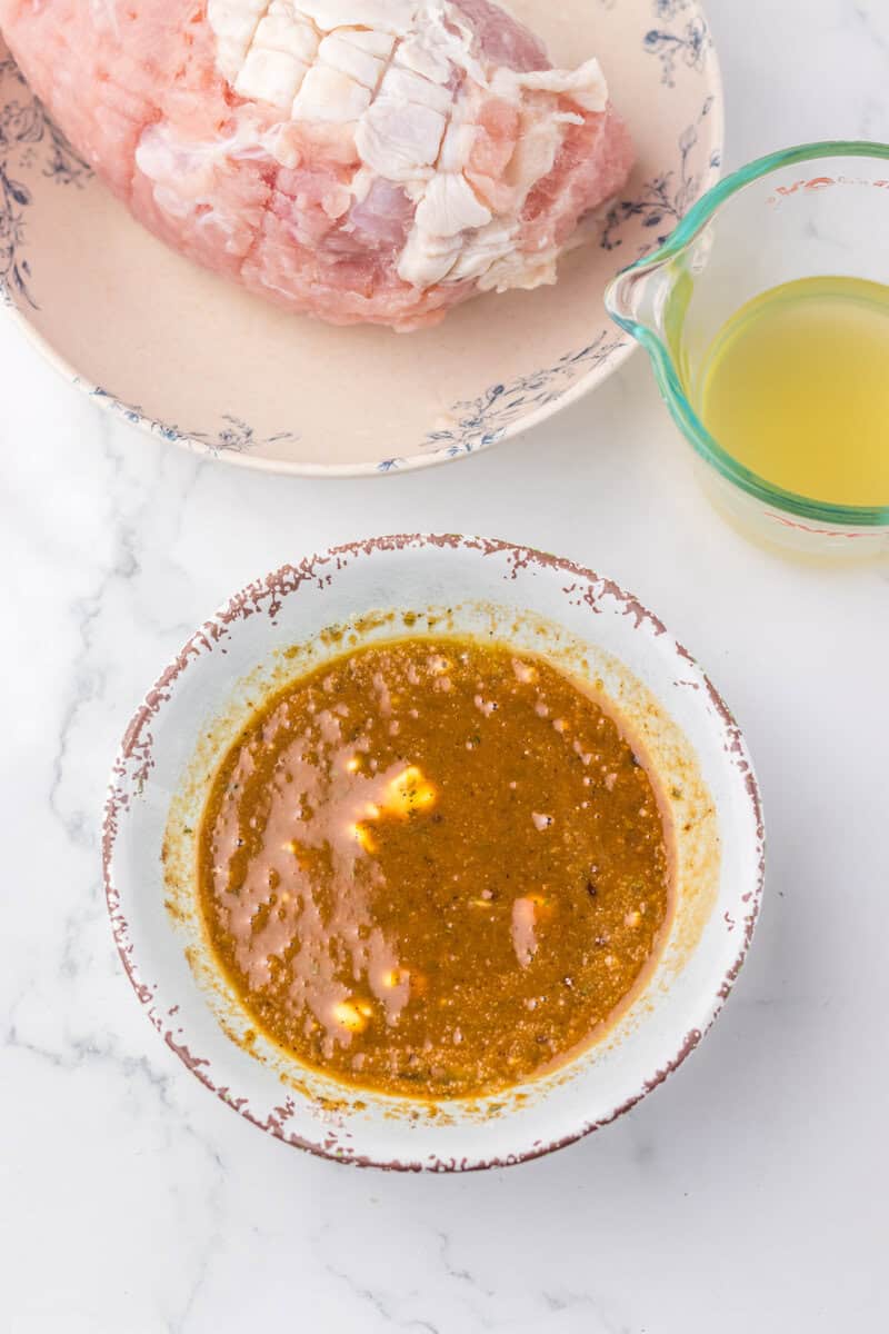 Mixed butter and seasonings in a glass bowl with a raw turkey breast nearby.