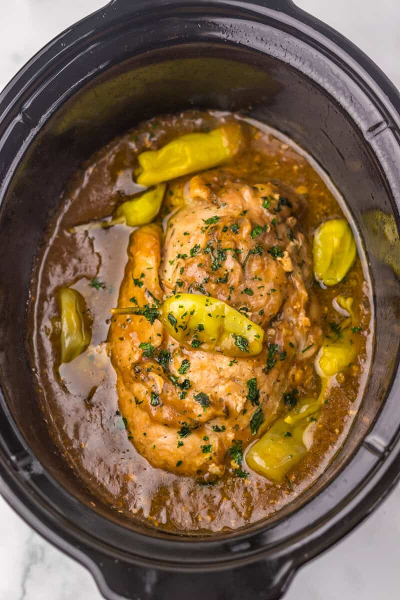 Crockpot Mississippi turkey breast in a slow cooker topped with pepperoncini peppers and surrounded by gravy.