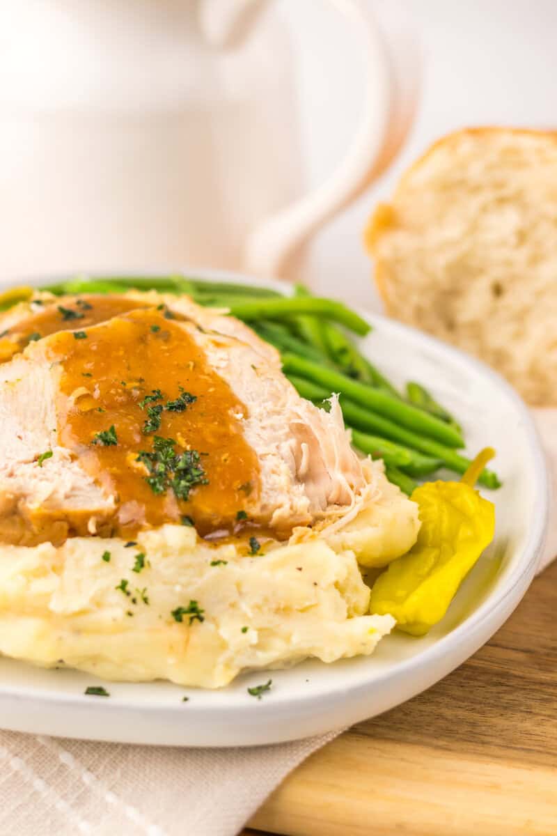 Sliced turkey breast with pepperonicini peppers, green beans, and gravy on a white plate.