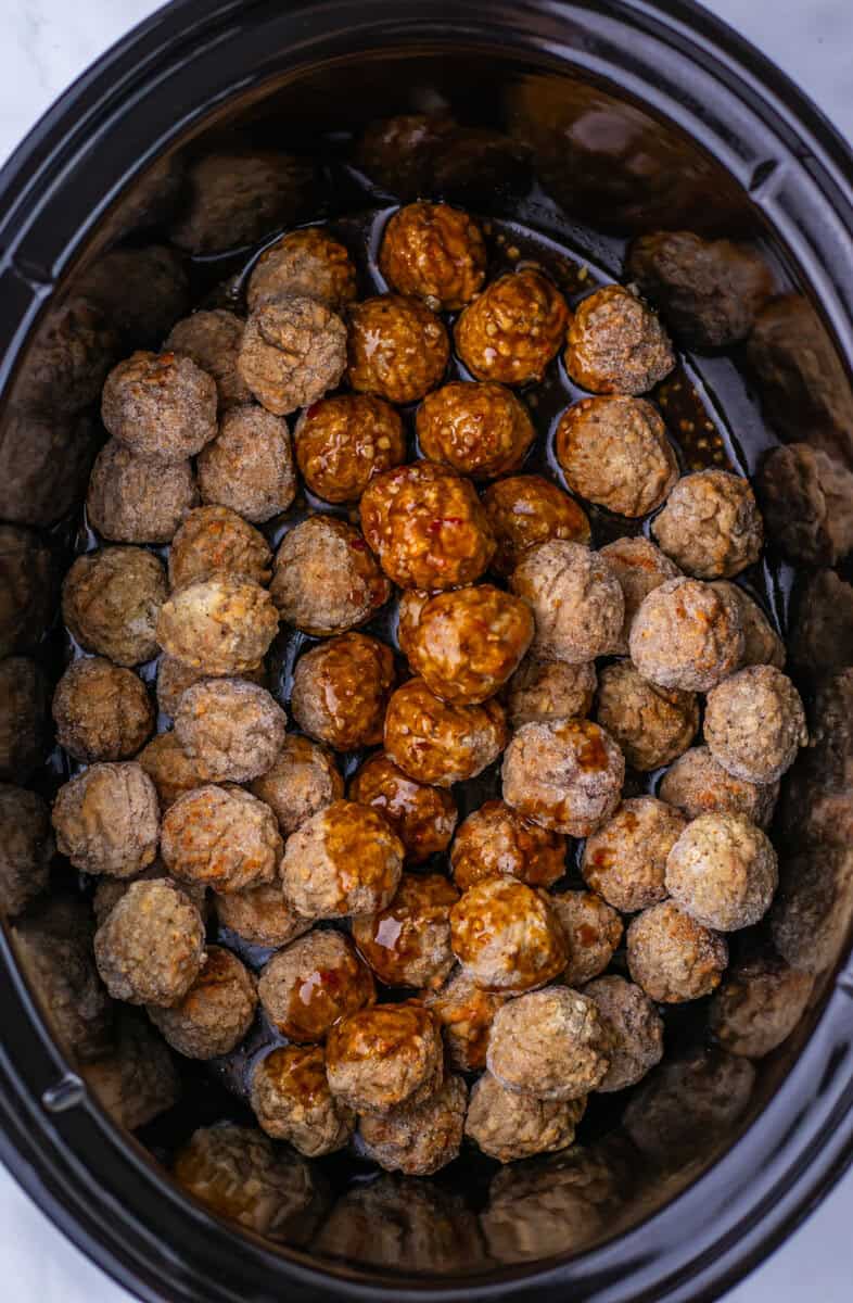 Meatballs in a slow cooker, with a row in the center covered in sauce while the rest remain unsauced.