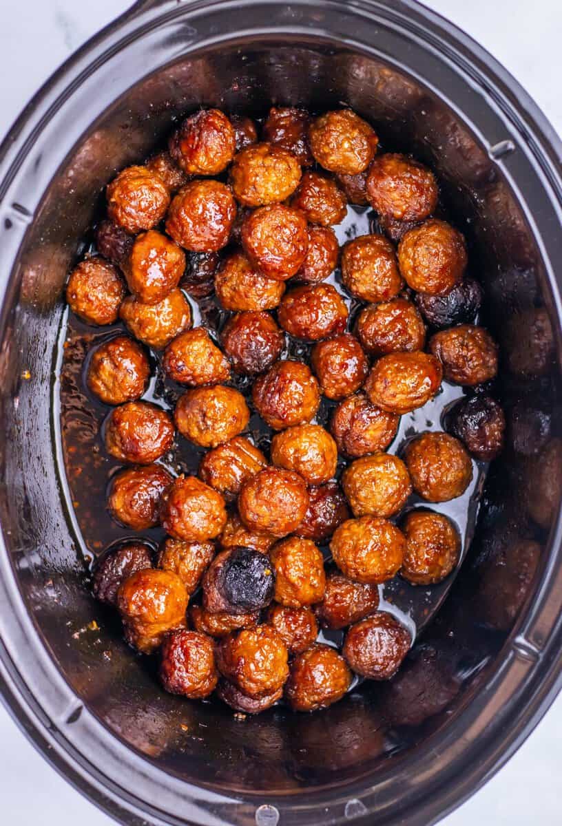 Meatballs coated in sauce are arranged in a single layer inside a black slow cooker.