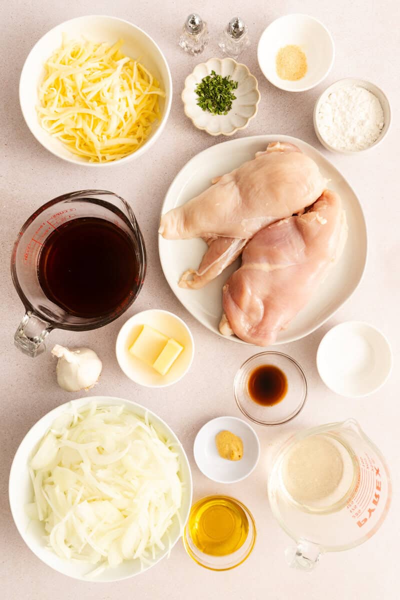 Raw chicken breasts, shredded cheese, sliced onions, beef broth, and spices in individual bowls on a white background.