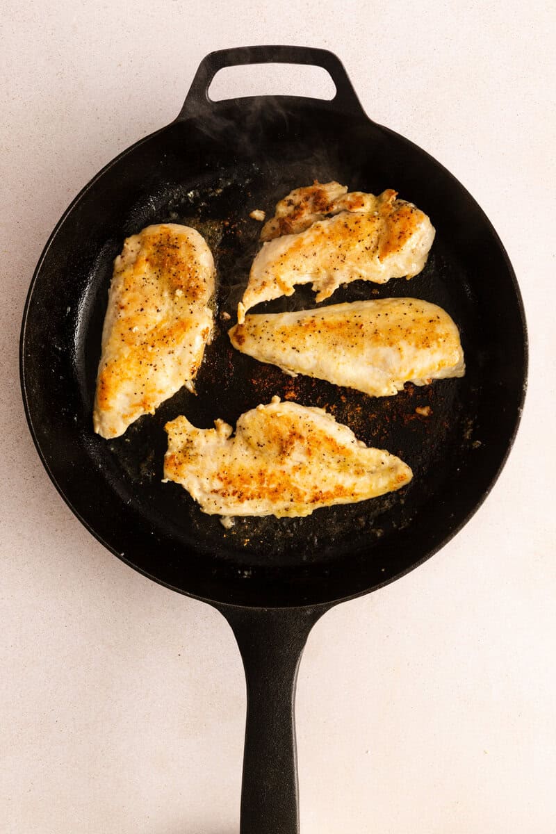 Chicken breast searing in a cast iron skillet.