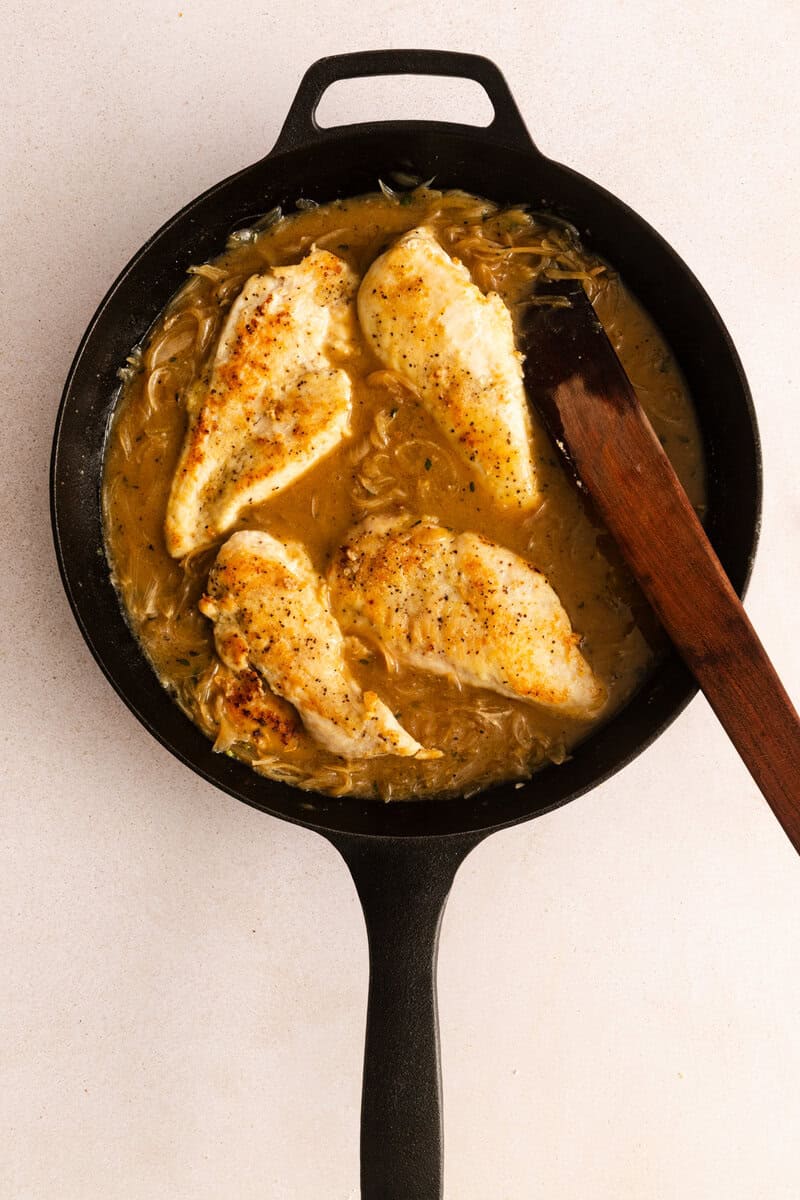 Cooked chicken breasts, caramelized onions, and brown sauce in a cast iron skillet.
