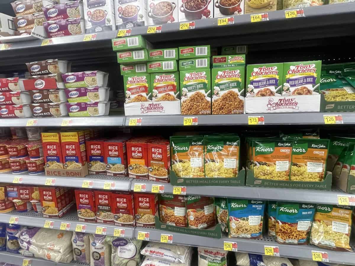 Grocery store shelves stocked with various rice mixes, including gluten free rice options from Tony Chachere’s, Rice-A-Roni, and Knorr brands, each with visible price tags.